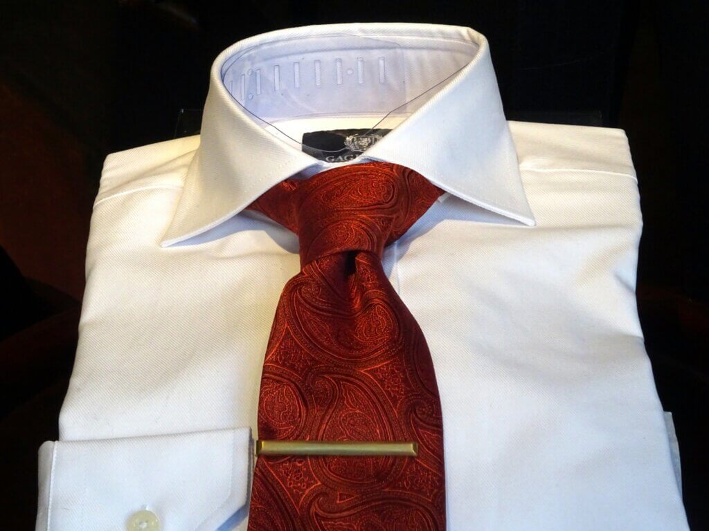 A white folded shirt with shiny red tie and a tie clip