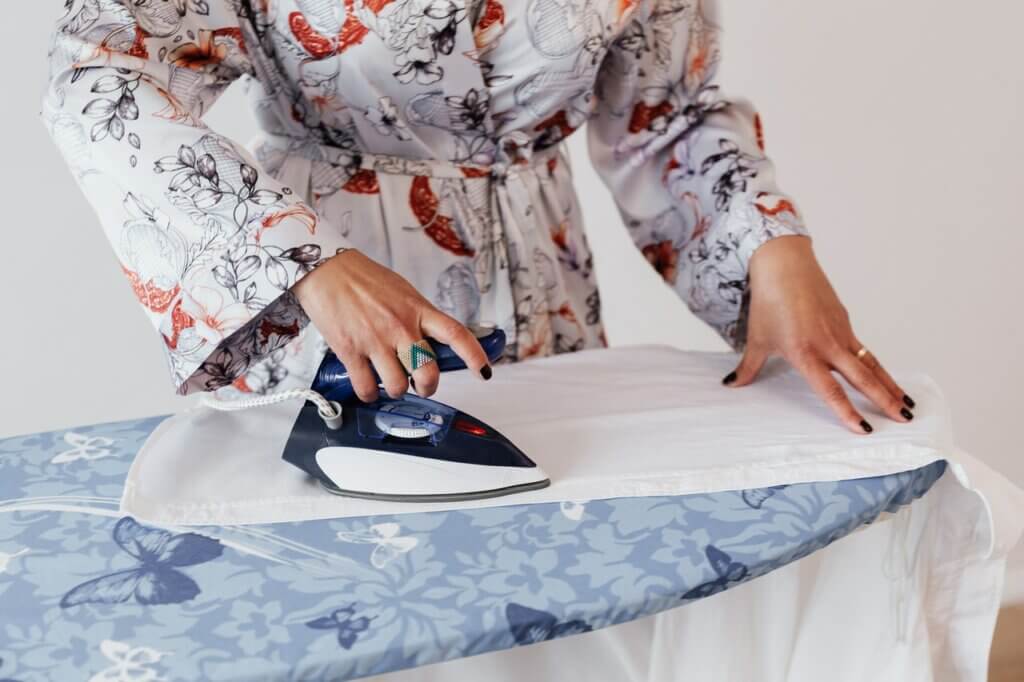 A lady ironing a shirt over the ironing top.