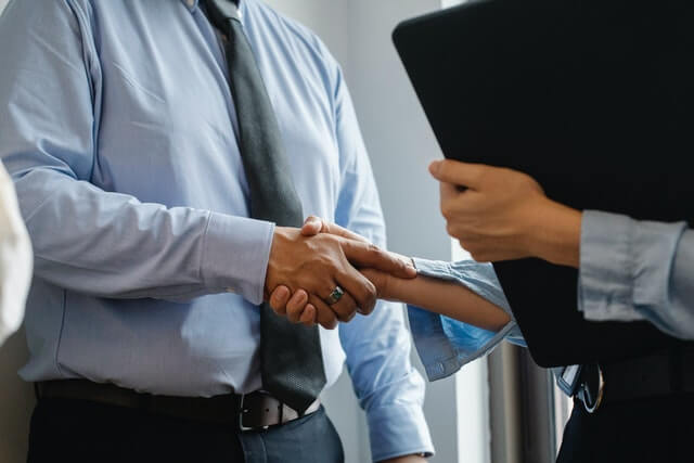 confident guy with a sky blue shirt and black tie shaking hands with a successful business deal