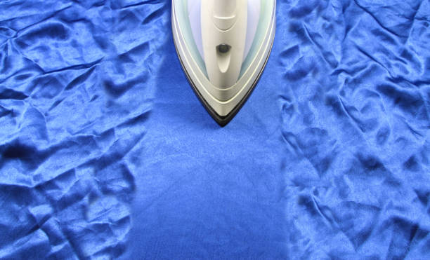Steam iron removing wrinkles from a blue silk cloth.